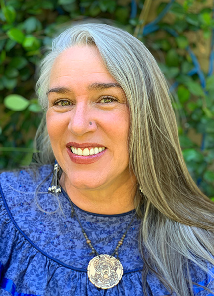Amy, a woman with long gray hair and a nose piercing, smiles at the camera
