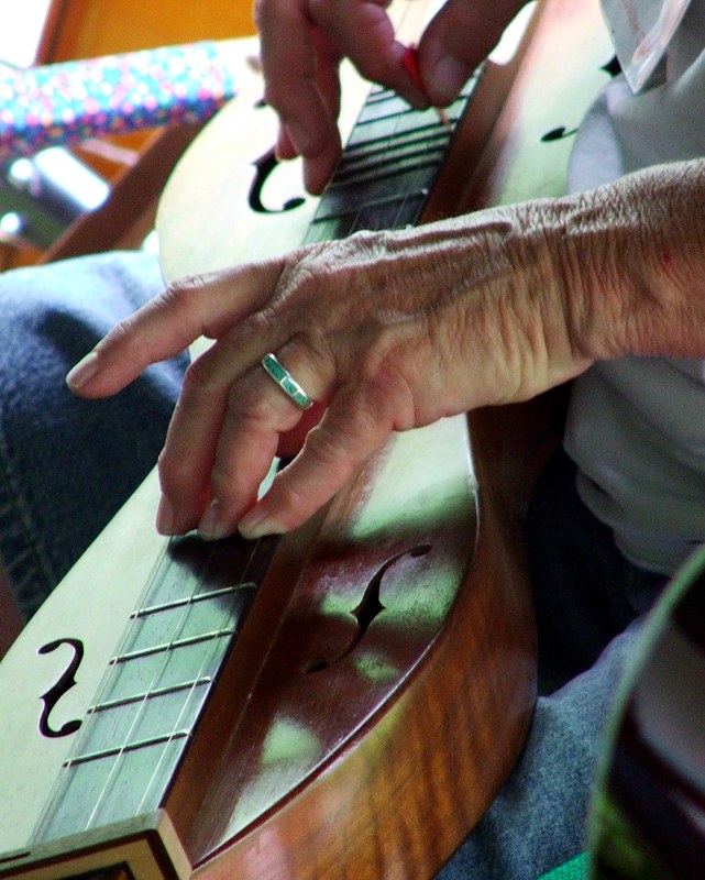 A close up of a person's hand on the strings of a dulcimer instrument