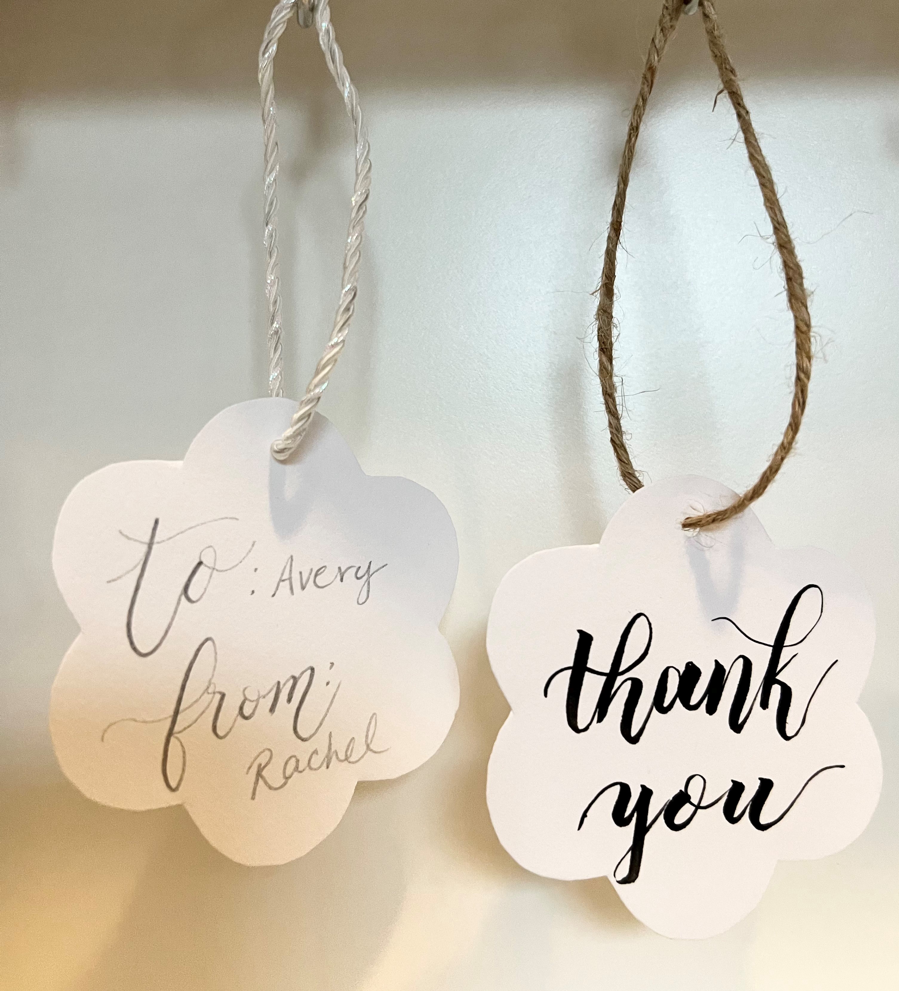 Two white flower-shaped gift tags with calligraphy black text