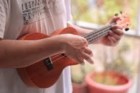 person holding a ukulele in front of their torso in front of a window