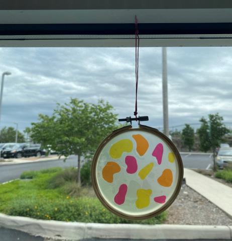 Pink, orange, and yellow round suncatcher hanging in a window