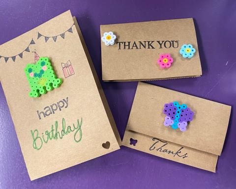 Three brown paper greeting cards with perler bead decorations