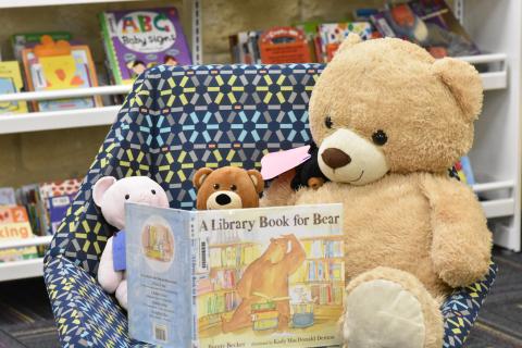 three stuffed bears sit in a chair "reading" a picture book