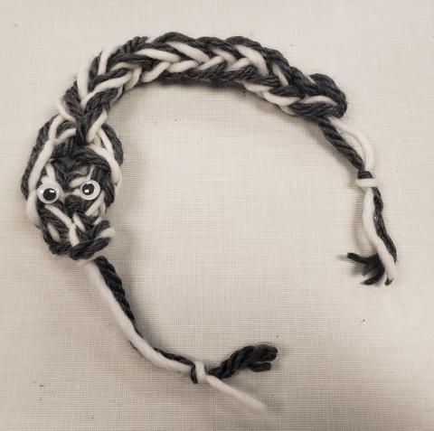 Small snake knitted from grey and white yarn with two googly eyes 