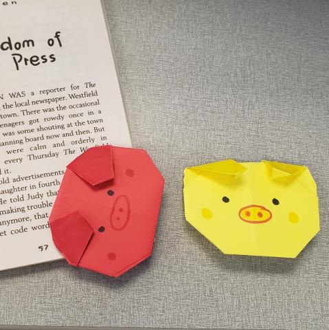red and yellow pig origami bookmarks, one marking spot in book and one laid out on table 