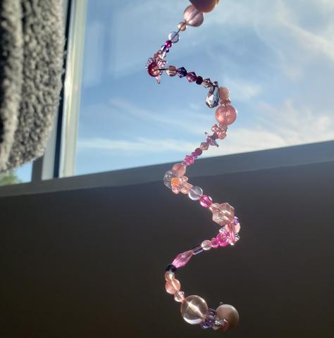 Beaded pink and purple suncatcher catching light by a bright window 