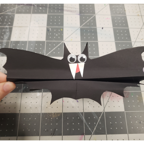 Black construction paper bat with googly eyes and two white fangs 