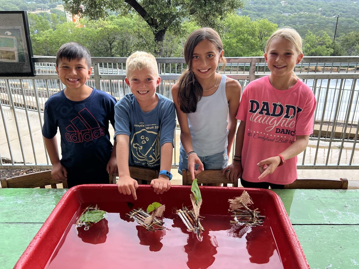 four kids with stick and leaf boats they created at the library